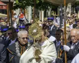 Procesja Bożego Ciała z monstrancją. Uczestnicy w strojach, wierni, policjanci.