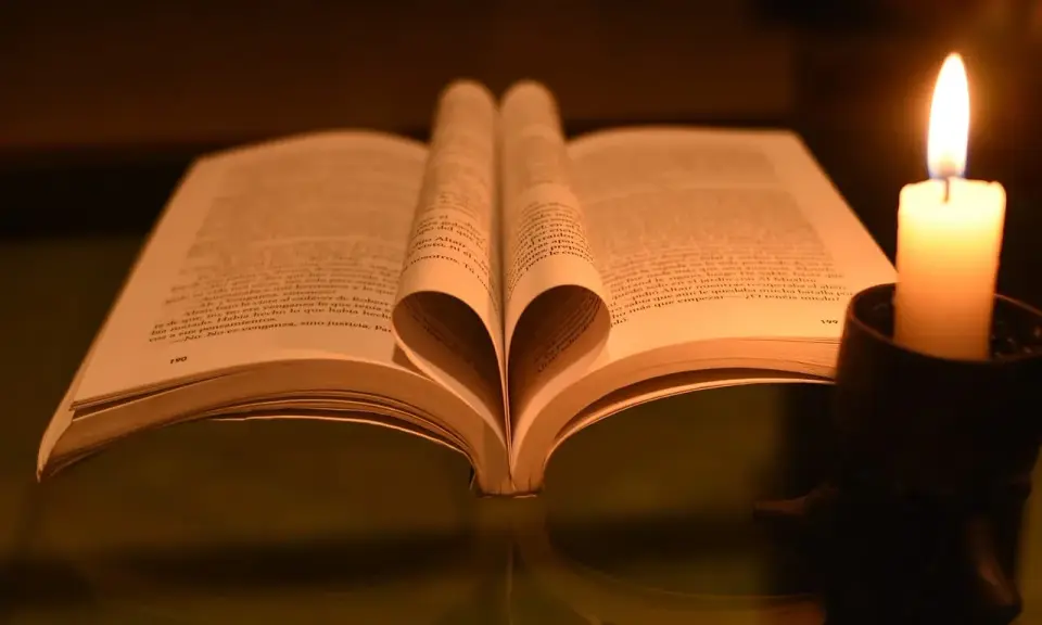 Otwarta księga z kartkami uformowanymi w serce, obok płonąca świeca. W świetle świecy czytam psalm 37 1-4.