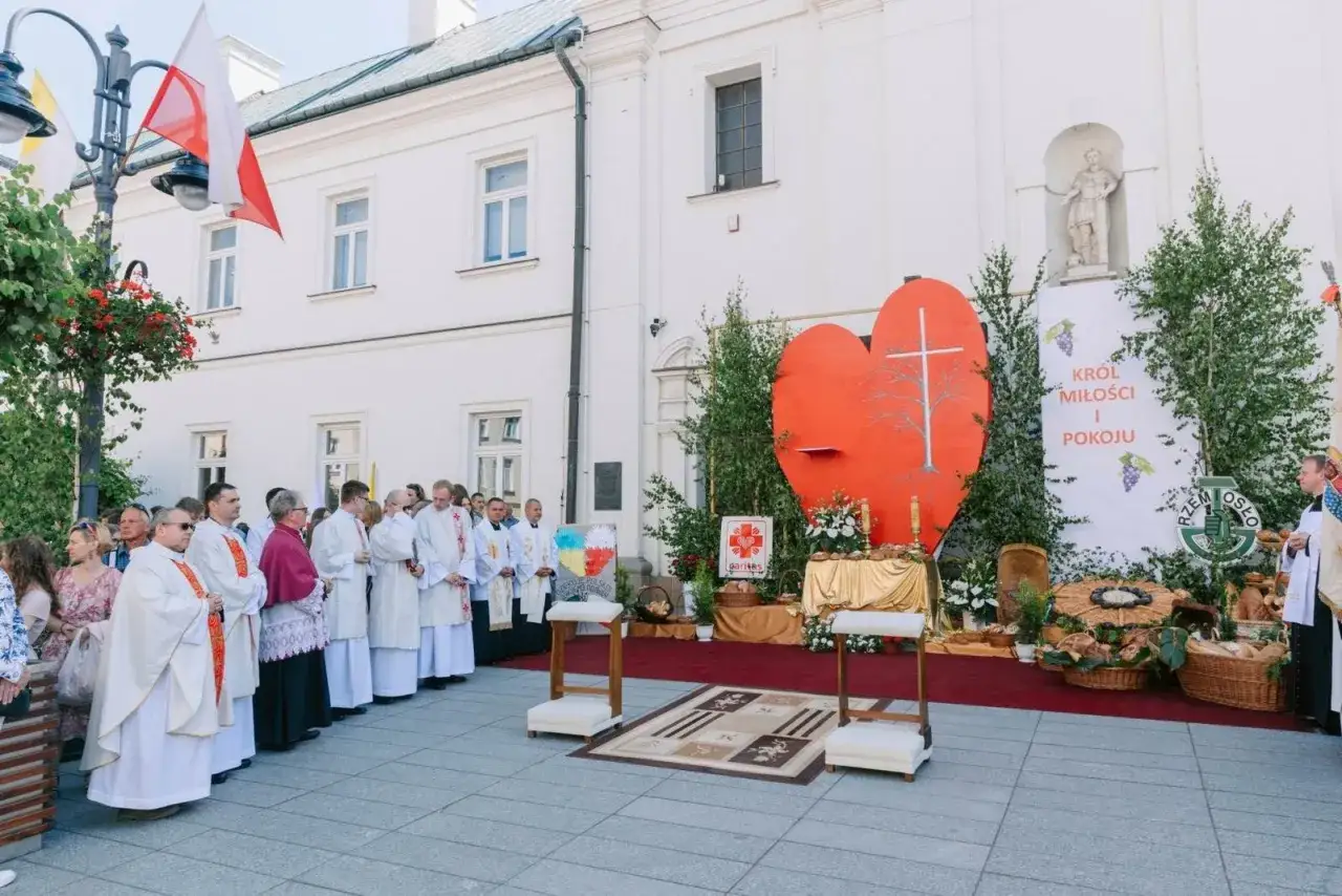 Uroczystość Bożego Ciała. Procesja z wielkim, czerwonym sercem i krzyżem. Kapłani w białych szatach.