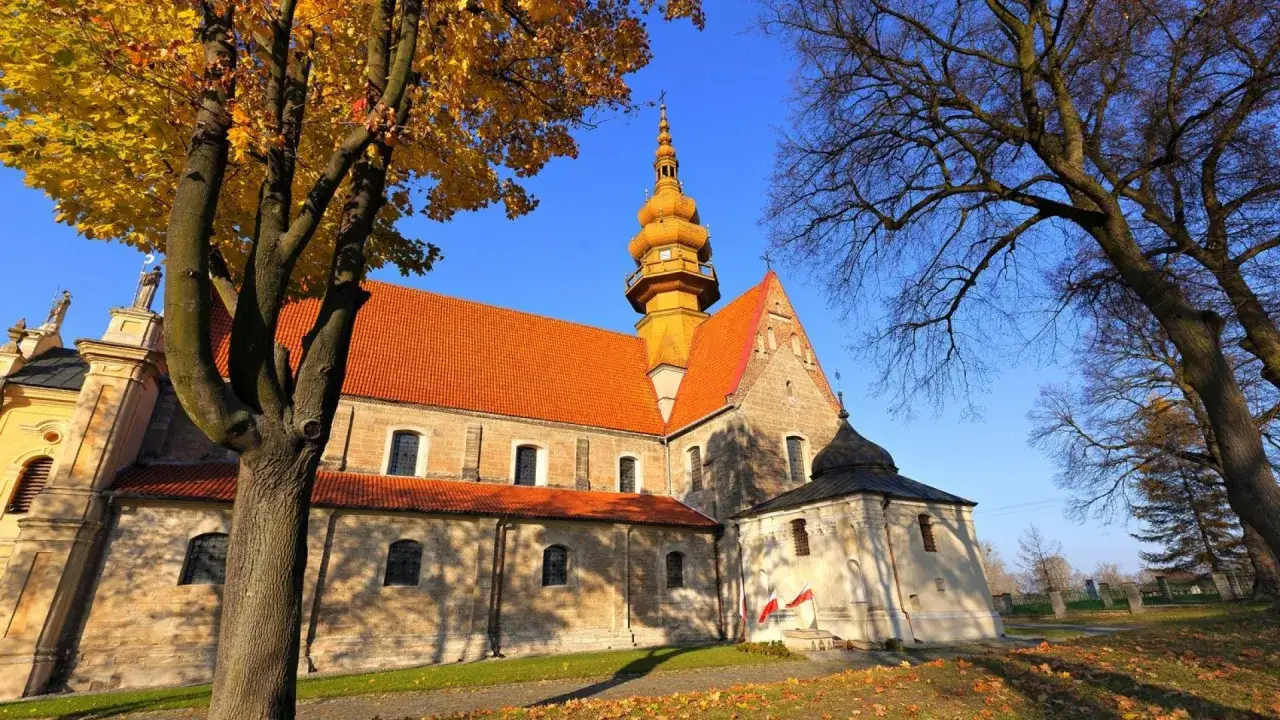 Kamienna świątynia z pomarańczowym dachem i złotą wieżą, otoczona jesiennymi drzewami. To kościół św. Zbigniewa.