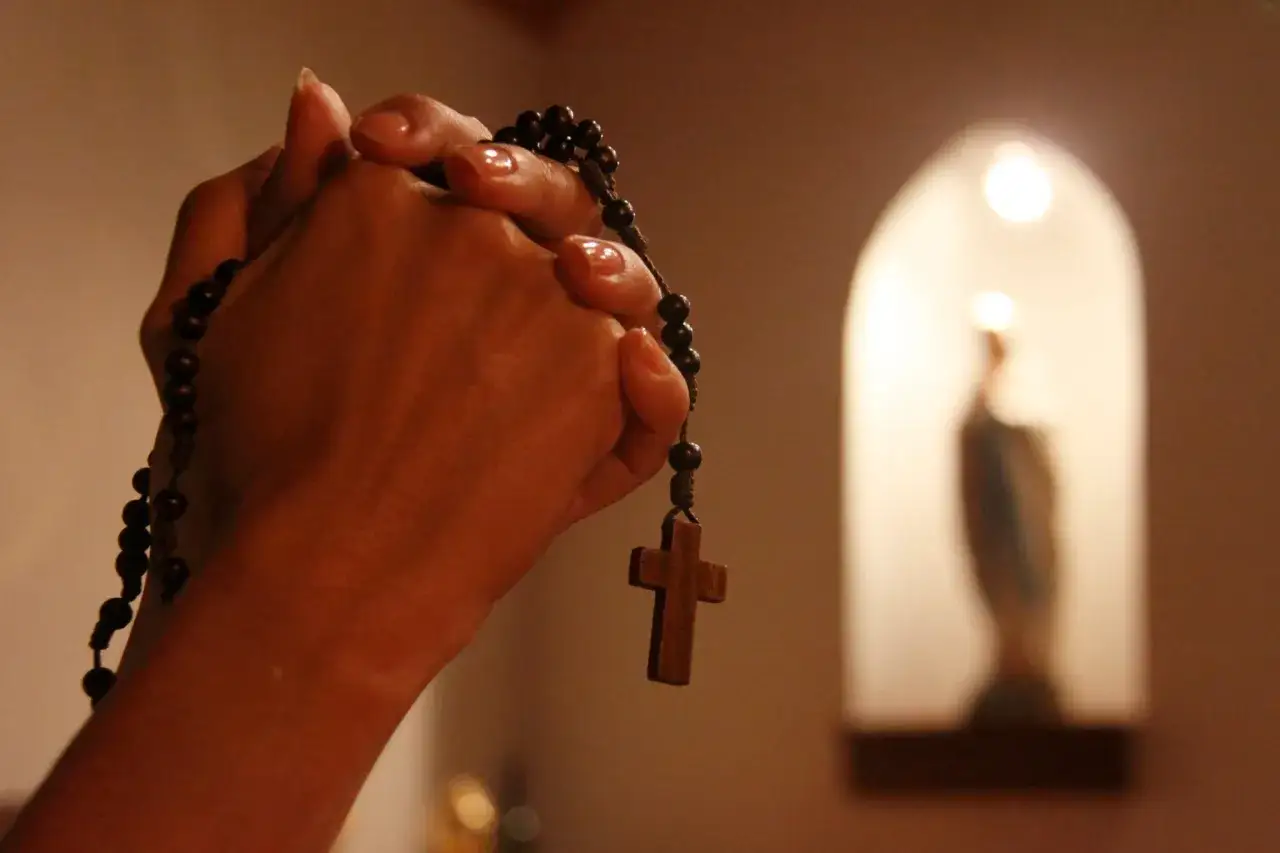 Dłonie z paciorkami różańca, w tle figura Matki Boskiej. Modlitwa do Maryi od spraw niemożliwych.